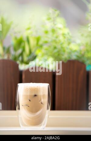 Eiskaffee mit Milch auf einem Holztisch mit unscharfen Kräuter im Hintergrund Stockfoto