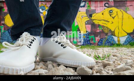 Damenfüße mit weißen Sneaker-Schuhen im Hüftstil. Städtische Straßengraffiti im Hintergrund. Mostar, Bosnien und Herzegowina. Stockfoto