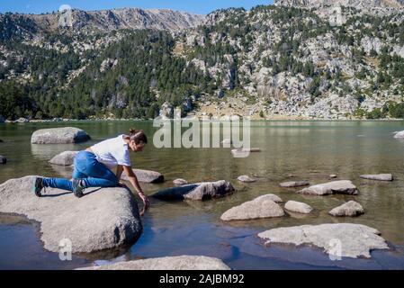 Volle Länge des Frau hockend auf Rock See gegen Berge Stockfoto