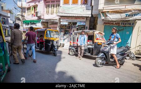 Udaipur, Indien - 04. März 2017: Ein junges Mädchen auf einem Roller wartet auf der Straße, besetzt durch Rikschas und zwei junge Kerle, die Rollen sind ein Stockfoto