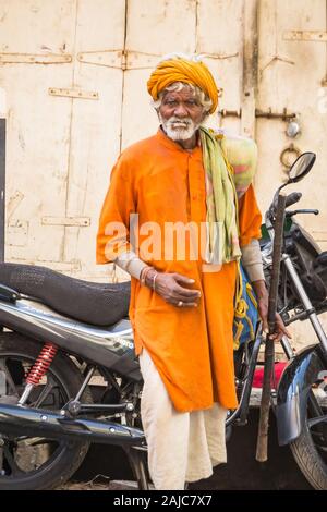Udaipur, Indien - 05.März 2017: Der alte Mann kreuzt die Straße. Er trägt traditionelle Kleidung der hellen orange Farbe. Stockfoto