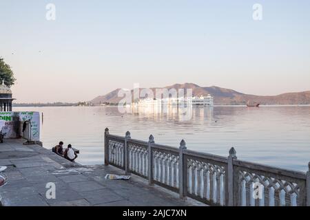 Udaipur, Indien - 05.März 2017: Zwei Kerle, die ihre Kleider waschen im See. Hinter ihrem Rücken ist ein schöner Blick auf das Taj Lake Palace. Stockfoto