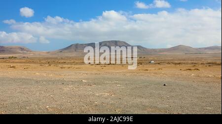 Trockene Böden unter weißen Wolken und blauer Himmel mit Bergen im Hintergrund Blick auf Fuerteventura Stockfoto