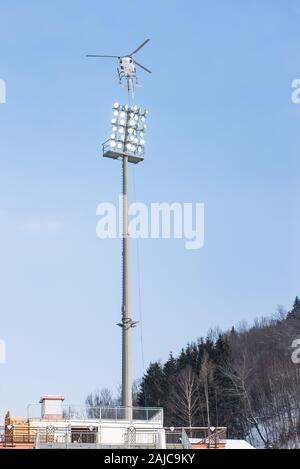 Hubschrauber mit der Ladung auf dem Hintergrund der blauen Himmel und Hügel mit Bäumen. Hohen Stahlmast mit Reflektoren. Stockfoto