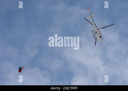 Eine tragende Hubschrauber blau, bewölkter Himmel. Cargo ausgesetzt auf ein langes Seil. Stockfoto