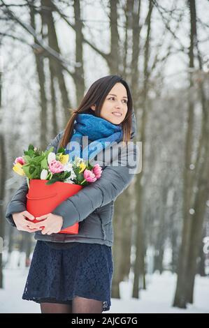 Das Mädchen hält in ihrer Hände rote Geschenkbox mit schönen Blumenstrauß blühen rosa, gelbe und weiße Tulpen und weissen Chrysanthemen Blumen als Geschenk f Stockfoto