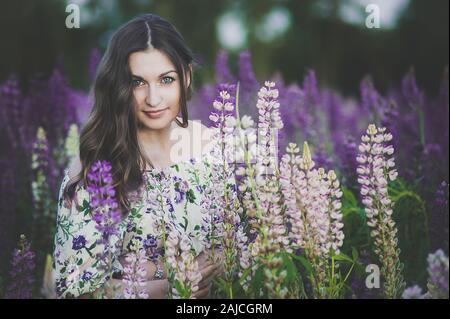 Portrait von schönen jungen Mädchen in Ultra Violett und Weiß Kleid mit einem Blumenstrauß von Lupine bei Sonnenuntergang auf dem Feld. Der Begriff der Natur und Romantik Stockfoto