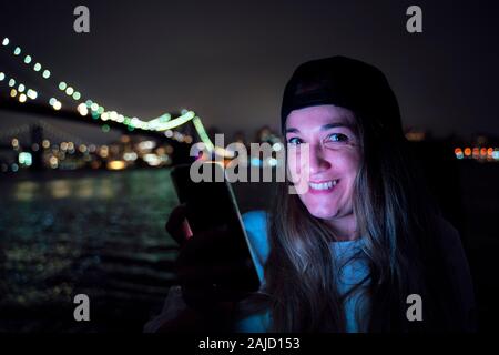 Attraktive Frau mit der Nachts Smartphone auf der Brooklyn Bridge Stockfoto