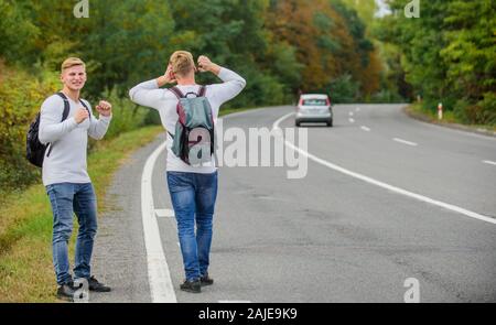 Anreise per Autostop. Hoffnungslos hitchhiker. Männer versuchen stop Auto. Zwillinge zu Fuß entlang der Straße. Wanderer Mann auf der Straße. Art des Reisens. Nur Freunde und Straße voran. das Gefühl der Freiheit. Mit Freunden unterwegs. Stockfoto