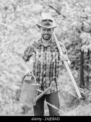 Baumpflanzung Tradition. Wachsende Pflanzen. Reifen Kerl Cowboy Hut mit Gießkanne und Schaufel. Arbor Day. Die Anpflanzung von Bäumen. Engagement und Verantwortung. Landwirtschaft Konzept. Pflanzen im Garten. Stockfoto