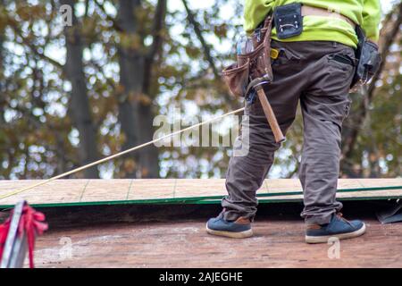 Ein Dach reparieren Mann steht auf einem Dach mit seinen Tools, bereit, ein undichtes Abschnitt über dieses Haus zu reparieren Stockfoto