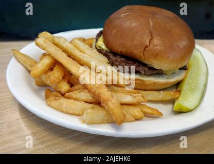 Saftige Hamburger mit Käse auf einem Brötchen, mit knusprigen Pommes frites und Dill Pickles Slice Stockfoto