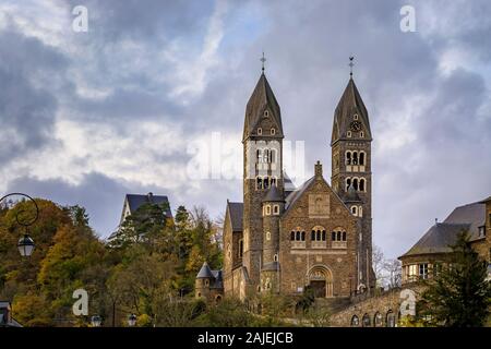 Fassade aus Stein der neo-romanischen Römisch-katholische Kirche der Heiligen kommen und Damien in Clervaux, Luxemburg durch einen Wald im Herbst umgeben Stockfoto