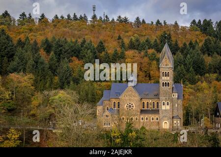 Fassade aus Stein der neo-romanischen Römisch-katholische Kirche der Heiligen kommen und Damien in Clervaux, Luxemburg durch einen Wald im Herbst umgeben Stockfoto