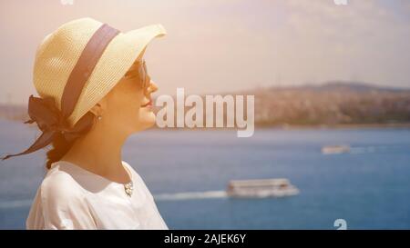 Träumen Frau in Sonnenhut steht halb Gesicht genießen Urlaub und schaut in die Ferne gegen blurry Landschaft closeup copyspace Stockfoto