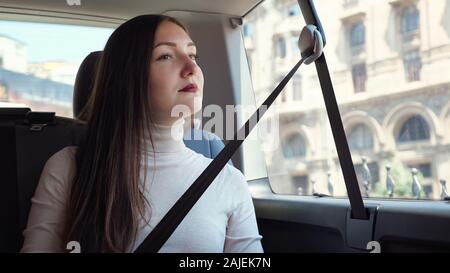 Anmutige Dame mit dunklen roten Lippen sitzt im Auto warten auf Treiber gegen architektonische Gebäude außerhalb Fenster closeup Stockfoto