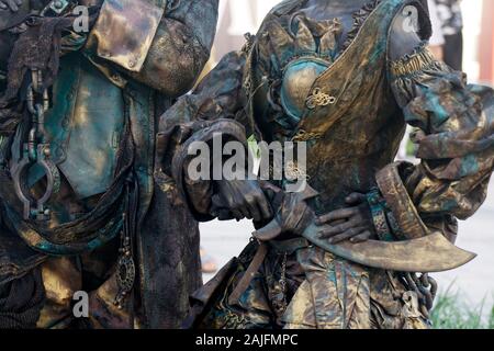 Details der lebende Statue von zwei Piraten. Frau und Mann in Bronze Kostüme mit Hüten und Waffen gekleidet darstellen als realistische menschliche Statue. Nahaufnahme Stockfoto