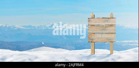 Holz- Wegweiser an der Spitze des Berges in den Schnee festgesteckt. Schneebedeckten Gipfeln im Hintergrund Stockfoto