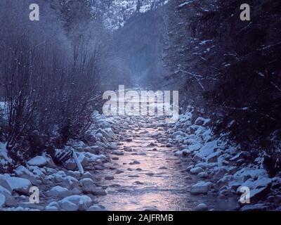 Eine Misty Mountain Stream fließt durch eine verschneite Landschaft. Die Bäume und Felsen sind mit Schnee bedeckt ein perfekter Winter ruhige Szene zu erstellen. Stockfoto