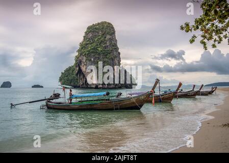 Phra nang Strand, Krabi, Thailand: Lange Leitboote, traditionelle thailändische Holzboote, thailändischer Mann und ko Rang nok Insel gegen eine dramatische bewölkte Stockfoto