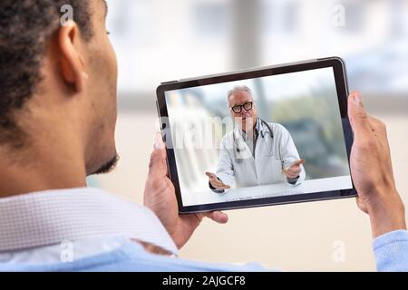 Virtuelle live Chat mit dem Patienten mit digitalen Tablet und ein Arzt über das Internet. In-home Care für eine junge männliche Patienten in der Telemedizin oder Telehealth, Stockfoto