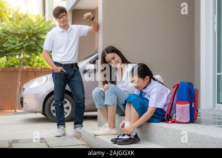 Asiatische Familie mit Vater, Mutter ihre Tochter Vorschulkinder Fernsehen in Uniform zu Ihren eigenen Schuhen infront von zu Hause für die Schule vorzubereiten Stockfoto