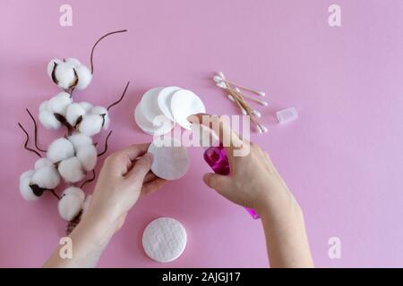 Wattepads zum Entfernen Make-up mit Frau Hände und Kosmetik auf rosa Hintergrund flach. Getrockneten Zweig der Baumwolle Blume. Stockfoto