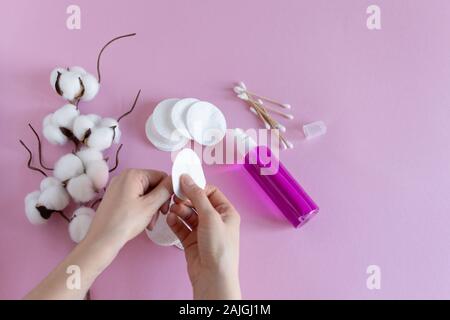 Wattepads zum Entfernen Make-up mit Frau Hände und Kosmetik auf rosa Hintergrund flach. Getrockneten Zweig der Baumwolle Blume. Stockfoto