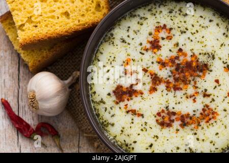 Hausgemachte türkische Joghurtsuppe, rote Paprika und Brot auf dem Holztisch Stockfoto
