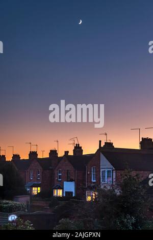 Northampton, Großbritannien. Bunte Himmel kurz nach Sonnenuntergang über den Dächern der Abington Gegend der Stadt, eine verblassende Viertel mond hoch am Himmel. Stockfoto