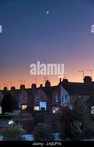 Northampton, Großbritannien. Bunte Himmel kurz nach Sonnenuntergang über den Dächern der Abington Gegend der Stadt, eine verblassende Viertel mond hoch am Himmel. Stockfoto