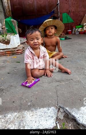 Zwei armen jungen asiatischen Jungen sitzen auf einem Bürgersteig vor der Provisorischen Schutz ihrer obdachlosen scavenger Familie in Kampong Cham, Kambodscha. Stockfoto