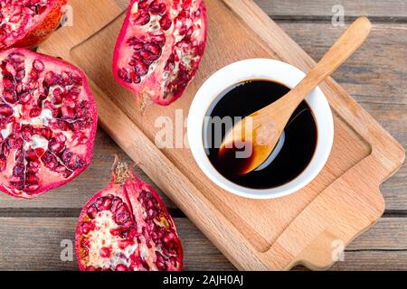 Hausgemachte Granatapfelsauce in einer Schüssel mit Löffel, frischer offener Granatapfel auf Holzgrund Stockfoto
