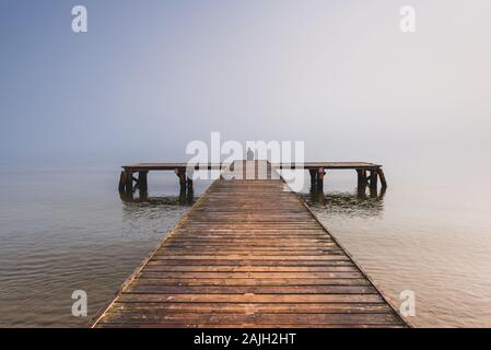 Eine Person, die am Ende des kleinen Pier saßen und auf den nebligen Meer. Stockfoto
