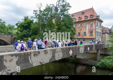 Menschen, die über die untere Brücke mit Gesichtern an der Seite in Bamberg, Oberfranken, Bayern, Deutschland laufen. Stockfoto