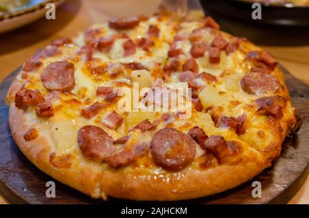 Pizza, Schinken, Käse, Wurst und Ananas auf einem hölzernen Fach Stockfoto