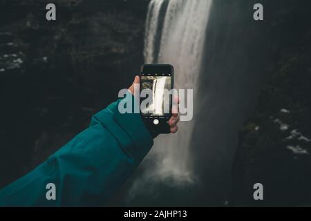 Junger Mann, der mit seinem Smartphone einen Wasserfall fotografiert Stockfoto