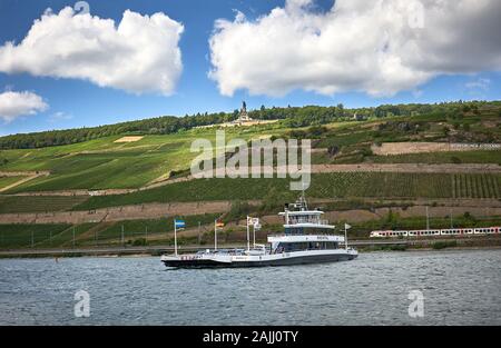 Mit der Autofähre fahren Passagiere von Bingen nach Rüdesheim über den Rhein, mit der Neiderwald-Gedenkstätte hoch oben auf dem Höhenrücken. Stockfoto