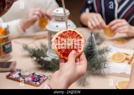 Woman's Hand mit einer Dekoration aus getrockneten Grapefruit. Getrocknete Orangen und cinamon auf dem verschwommenen Hintergrund. Girls Party oder Tagung. Stockfoto