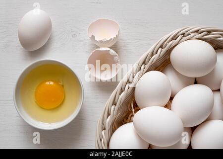 Detail der weißen Huhn Eier in einem Korb und gebrochene Ei in eine weiße Keramik Schüssel. Ansicht von oben. Stockfoto