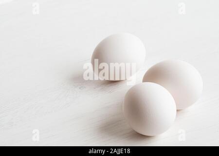 Ganze drei weiße Eier auf weiß lackiertes Holz isoliert. Platz für Text. Stockfoto