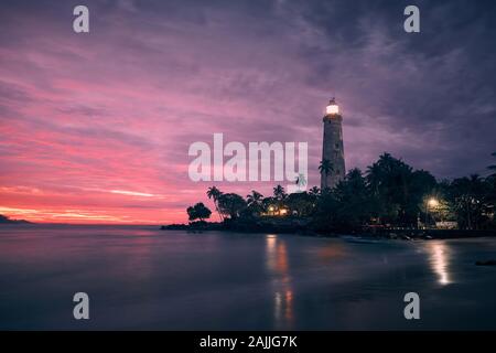 Beleuchtete Leuchtturm in der Mitte von Palmen gegen dramatische Himmel. Südküste von Sri Lanka an Bunte sunrise. Stockfoto