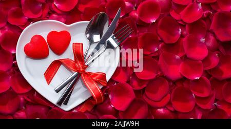 Rosenblätter auf herzförmige Platte mit Messer und Gabel, Valentines Tag essen Hintergrund Stockfoto