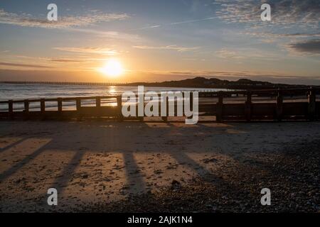 Schönen Sonnenuntergang Littlehampton Meer, Sonne werfen lange Schatten am Sandstrand, wie es auf den Horizont gleiten. Stockfoto