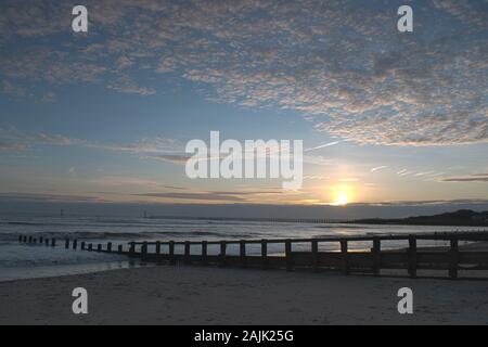 Sonnenuntergang auf Littlehampton Küste im Januar, als die Sonne taucht hinter Wolke am Horizont, die schönen Farben auf den Wolken. Stockfoto