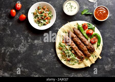 Türkische Adana Kebab mit frischem Gemüse auf Fladenbrot und Soße über schwarzen Stein Hintergrund. Ansicht von oben, flach Stockfoto