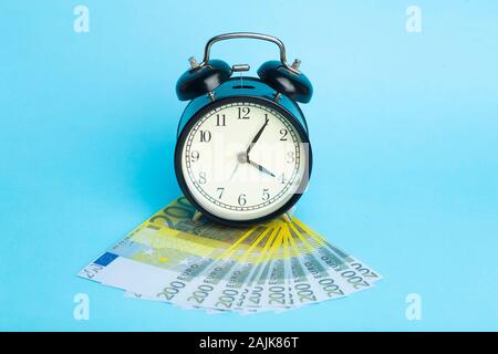 Zeit und Geld. Euro Bargeld und Wecker auf blauem Hintergrund. Stockfoto