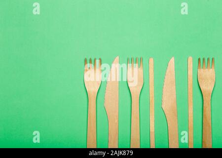 Hölzerne Gabeln und Messer für Lebensmittel in einem Pappbecher auf einem farbigen Hintergrund. Umweltfreundliches Einweggeschirr ohne Kunststoff. Stockfoto