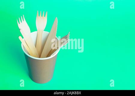 Holz- Gabel, Messer und Löffel für Lebensmittel in einem Pappbecher auf einem farbigen Hintergrund. Umweltfreundliches Einweggeschirr ohne Kunststoff. Stockfoto