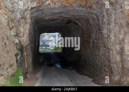 Die einspurige Doane Robinson Tunnel auf Iron Mountain Road mit Vorsicht Zeichen und einen Blick auf den Mount Rushmore im Hintergrund. Stockfoto